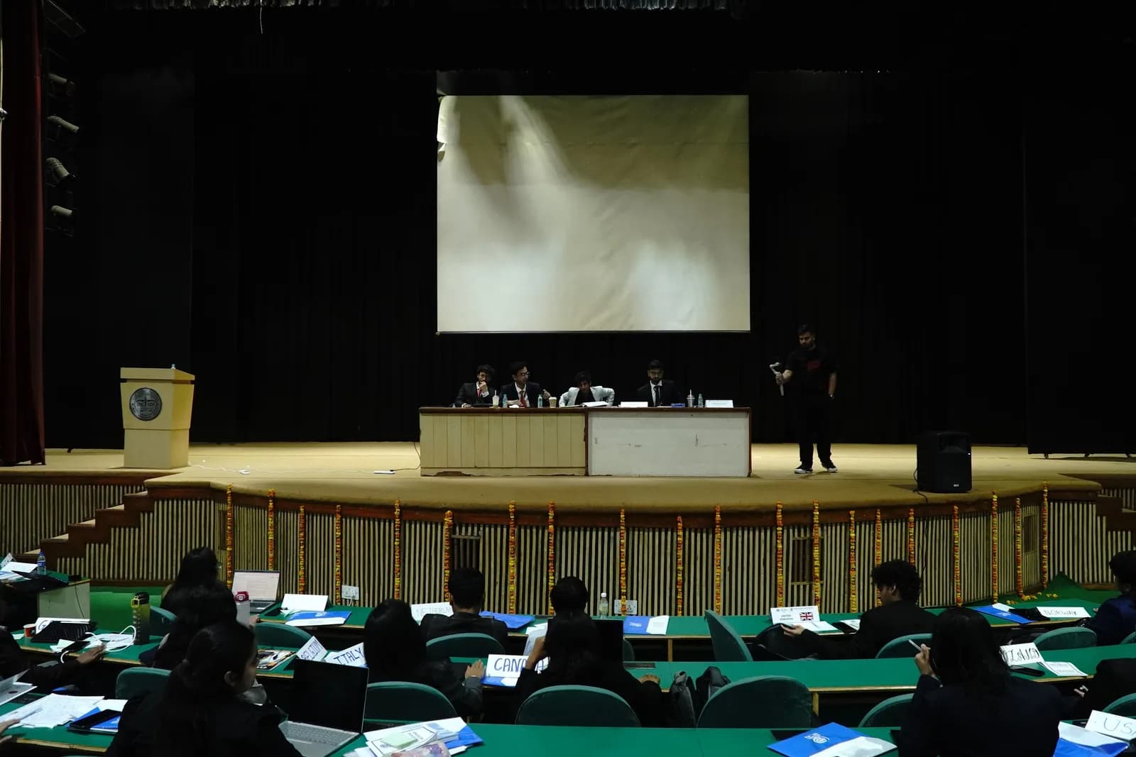 The conference auditorium seen from the back, delegates at their desks facing the dais
